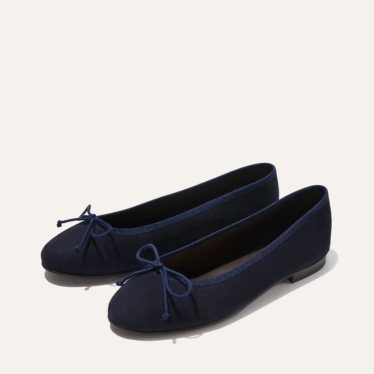 The Demi - Navy Suede by margaux-development: navy blue ballet flats handmade in Spain, featuring rounded toes and small bows, shown on a light background.
