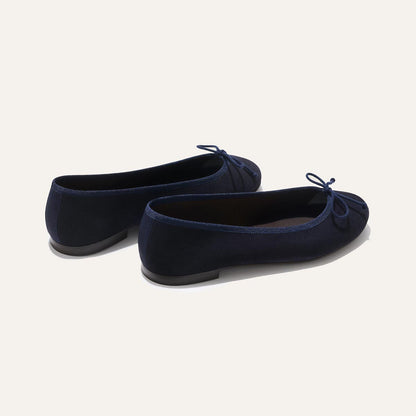 The Demi - Navy Suede by margaux-development: handmade navy blue ballet flats from Spain, featuring small bows on the toes, shown from a rear side angle on a plain light background.