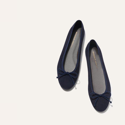 A pair of The Demi - Navy Suede ballet flats by margaux-development, handmade in Spain with small toe bows, displayed side by side on a light off-white background.