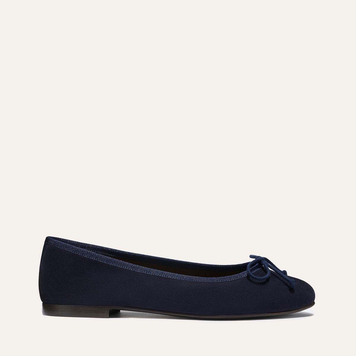 The Demi - Navy Suede by margaux-development is a handmade Spanish ballet flat in navy blue suede, featuring a small toe bow, rounded front, and black flat sole, shown in profile on a plain light background.