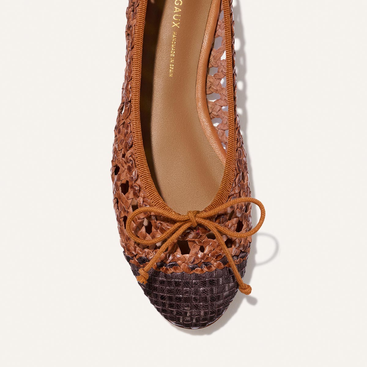 Brown woven ballet flat shoe with a decorative bow on a white background