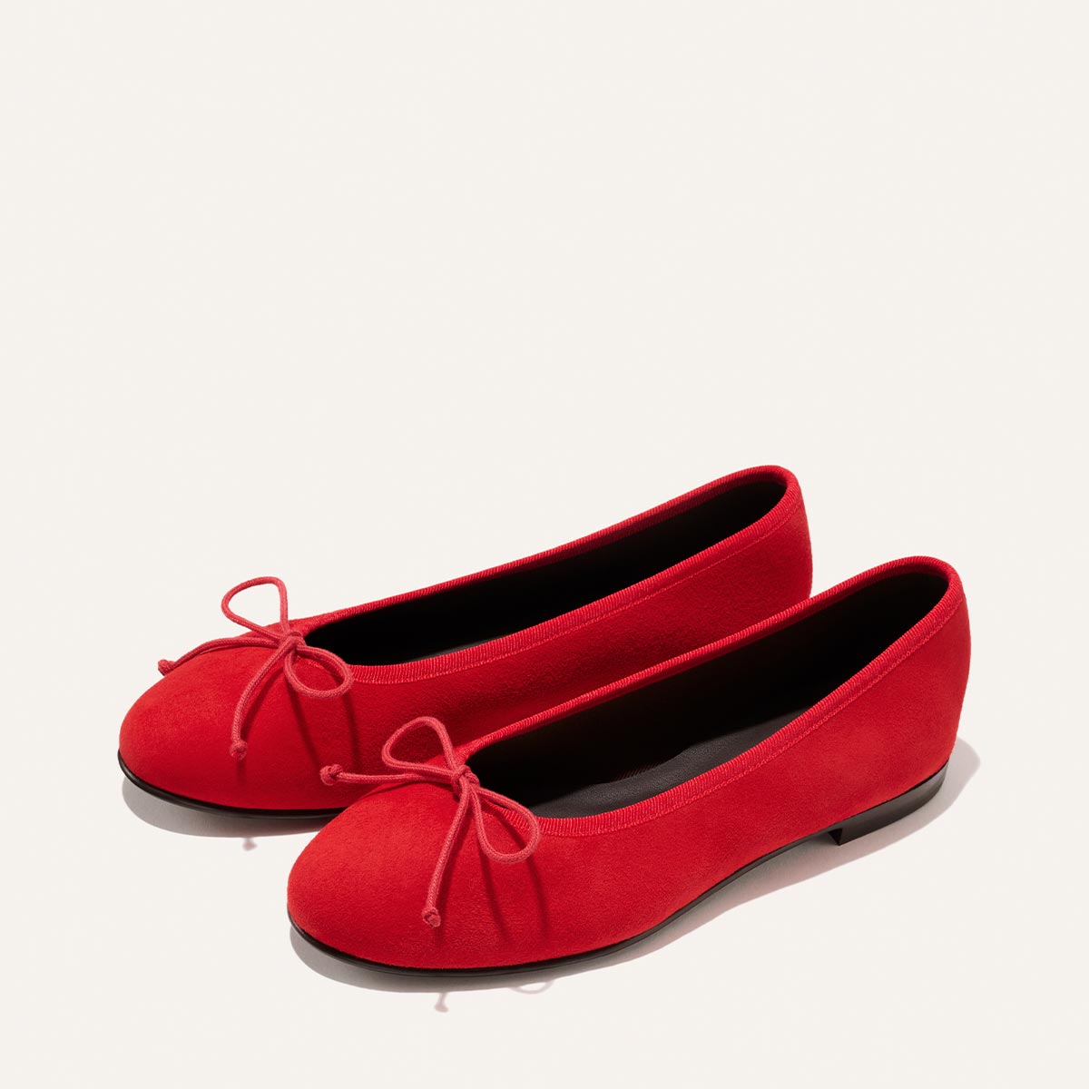 The Demi - Tomato Suede by Margaux: bright red ballet flats with rounded toes and delicate bows, handmade in Spain, displayed on a plain light background.
