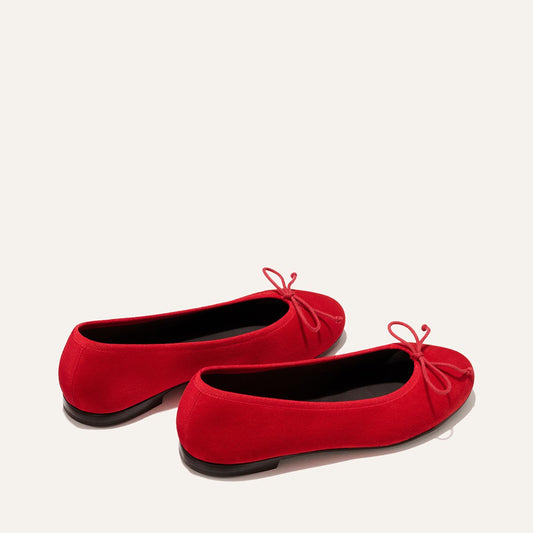 The Demi - Tomato Suede by Margaux: handmade in Spain, these bright red ballet flats feature small bows on the toes and are shown against a plain light background.