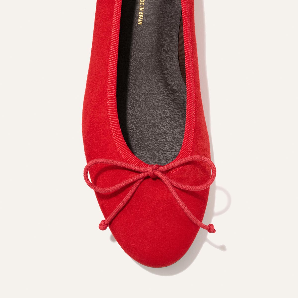 The Demi - Tomato Suede by Margaux: a vibrant red suede ballet flat, handmade in Spain, with a rounded toe and front bow, displayed from above on a light background.