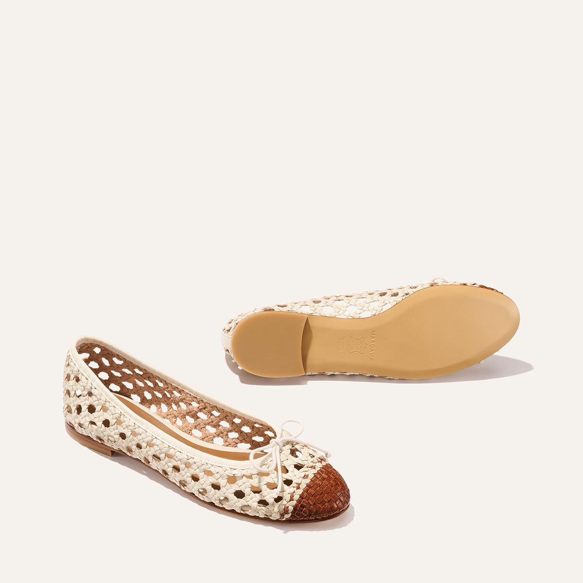 The Demi - Ecru and Saddle Woven Leather by Margaux features cream woven ballet flats with brown closed toes, small top bows, and flat beige soles, shown against a plain light background.