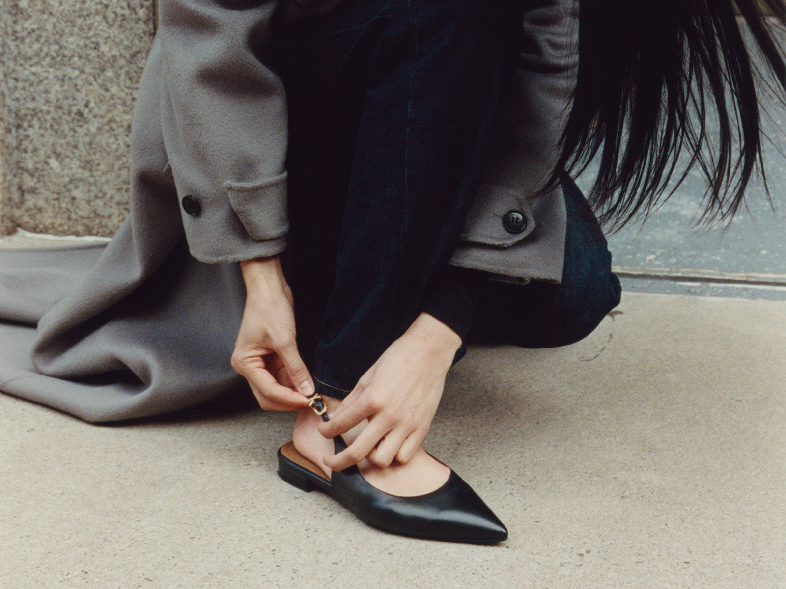Person adjusting a black flat shoe on a sidewalk