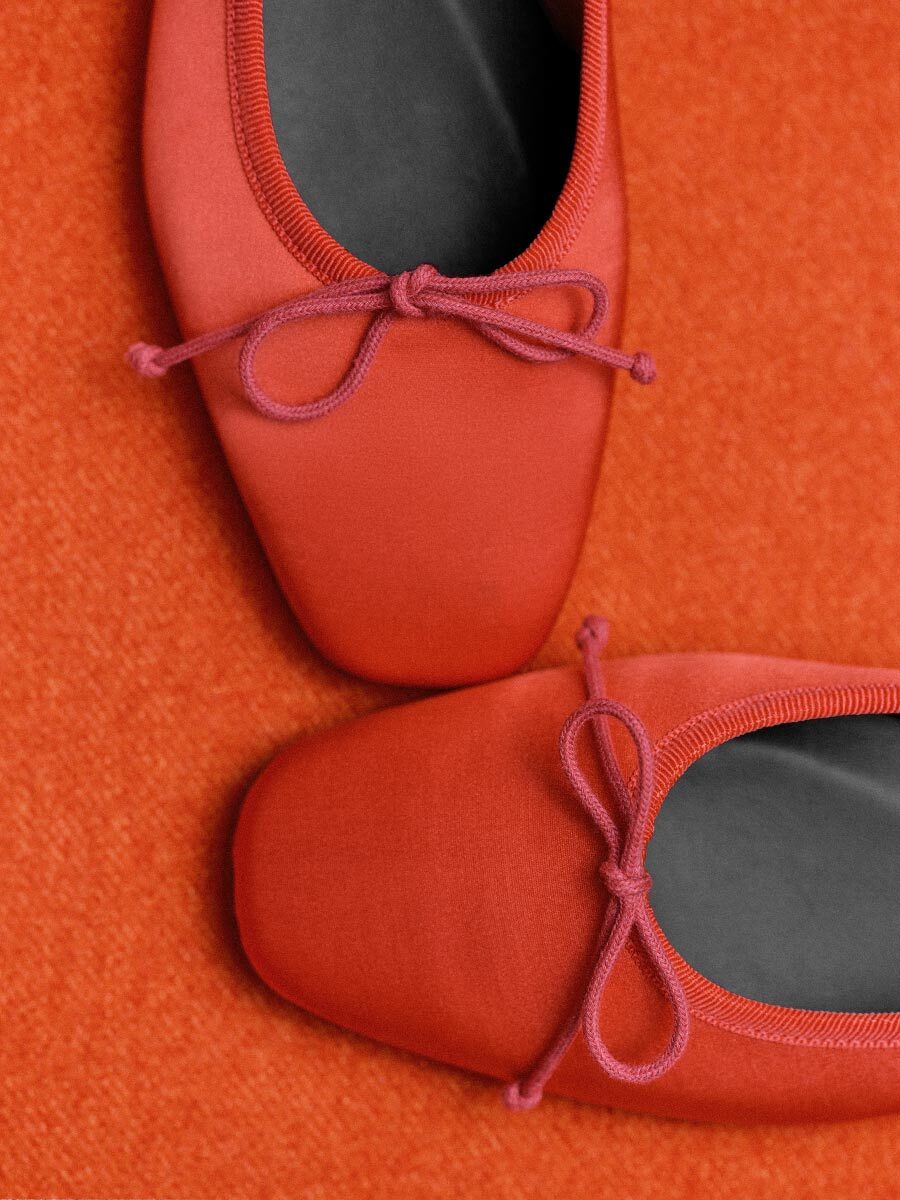 Red ballet shoes with pink laces on an orange background