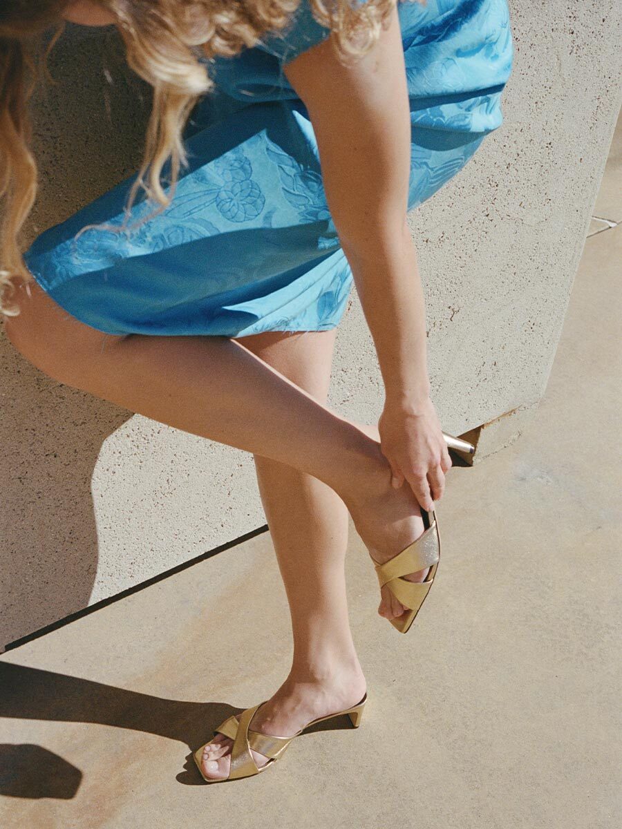 Person wearing a blue dress and gold sandals on a concrete surface