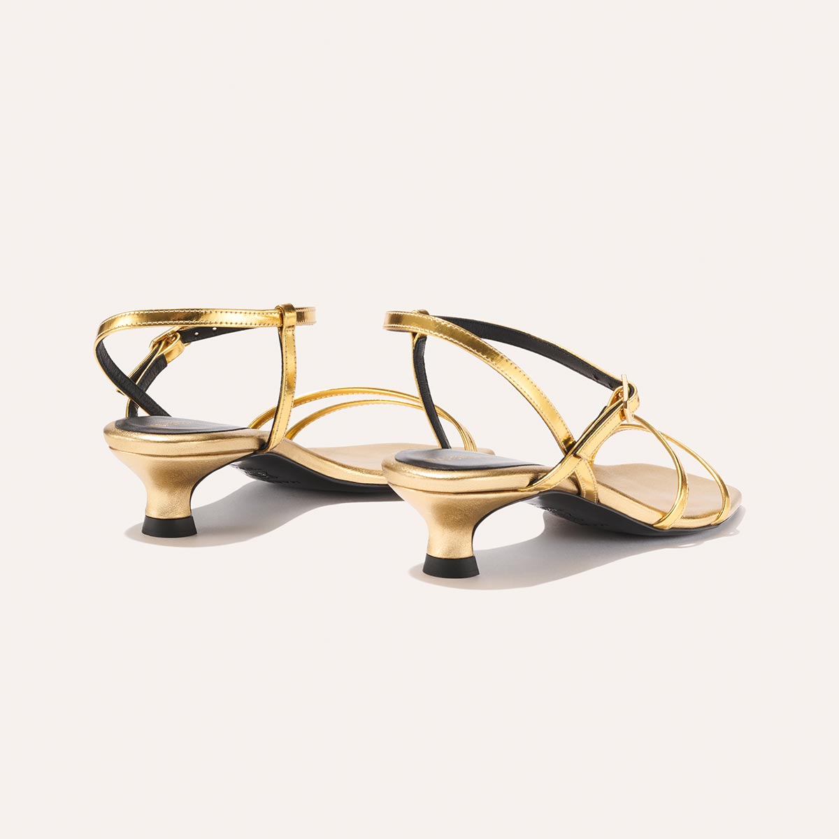 The Dylan Sandal - Gold Mirror by margaux-development features gold strappy heels with low, flared heels and ankle straps, shown against a plain light background.