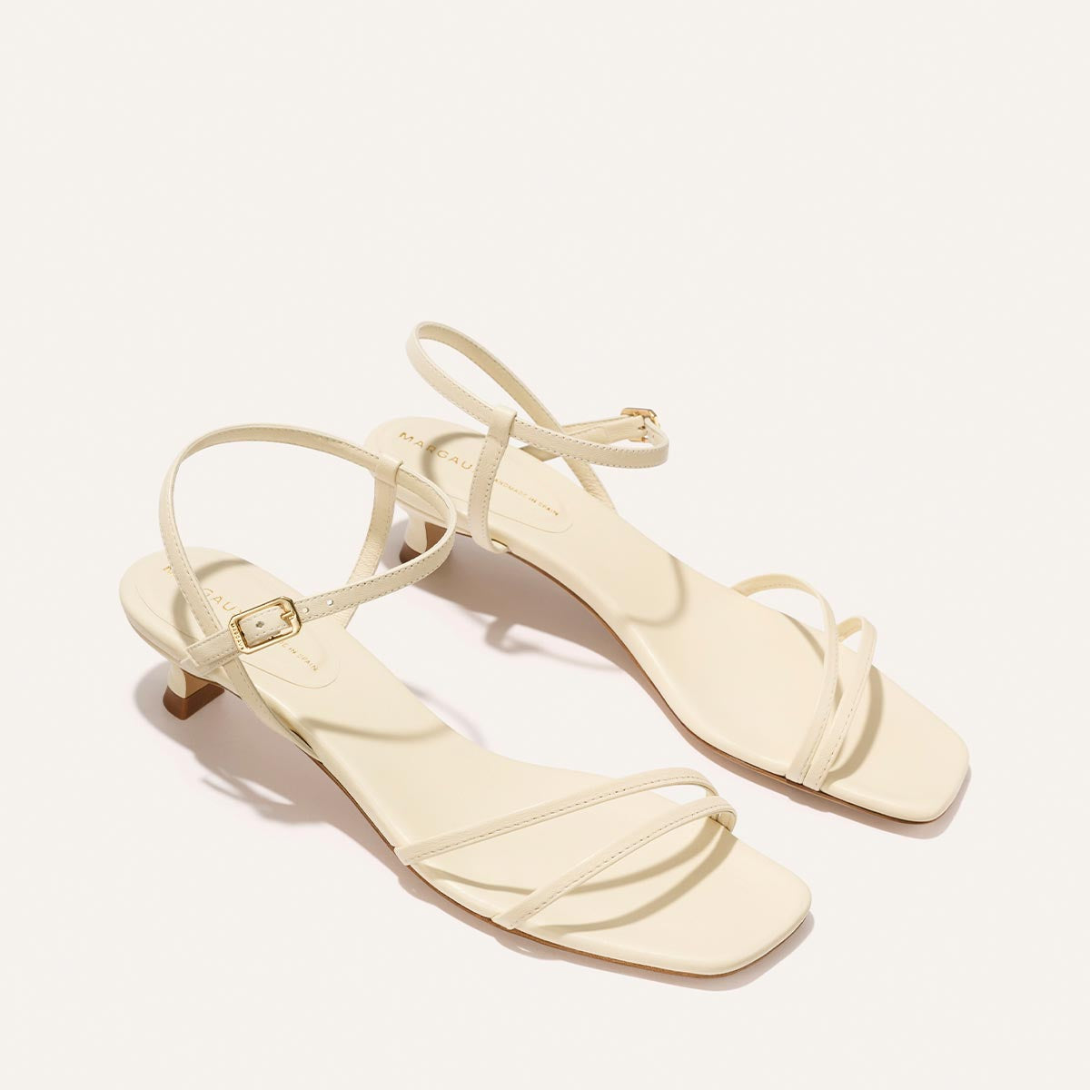 Pair of cream-colored high-heeled sandals on a light beige background