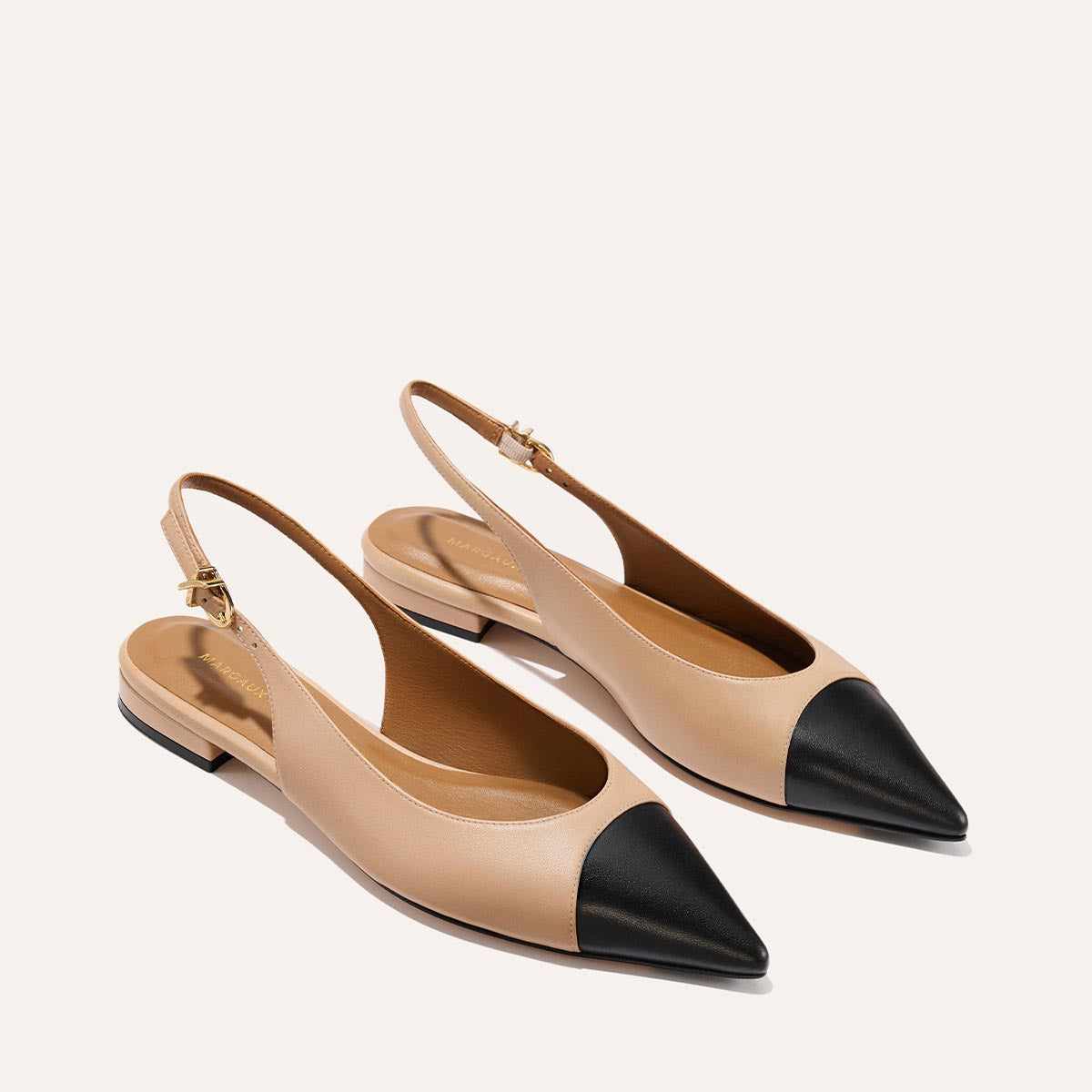 The Elise - Dune and Black Nappa by margaux-development are beige slingback flats with black toe caps, leather soles, and low heels, displayed on a light background.