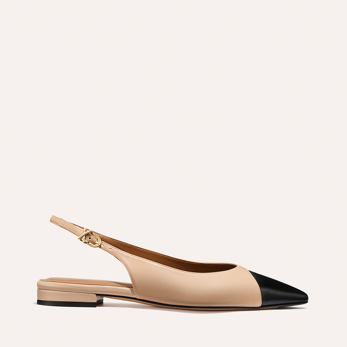 The Elise - Dune and Black Nappa by margaux-development is a beige pointed-toe slingback flat with a black cap, low heel, gold buckle strap, and leather sole, shown on a simple light background.