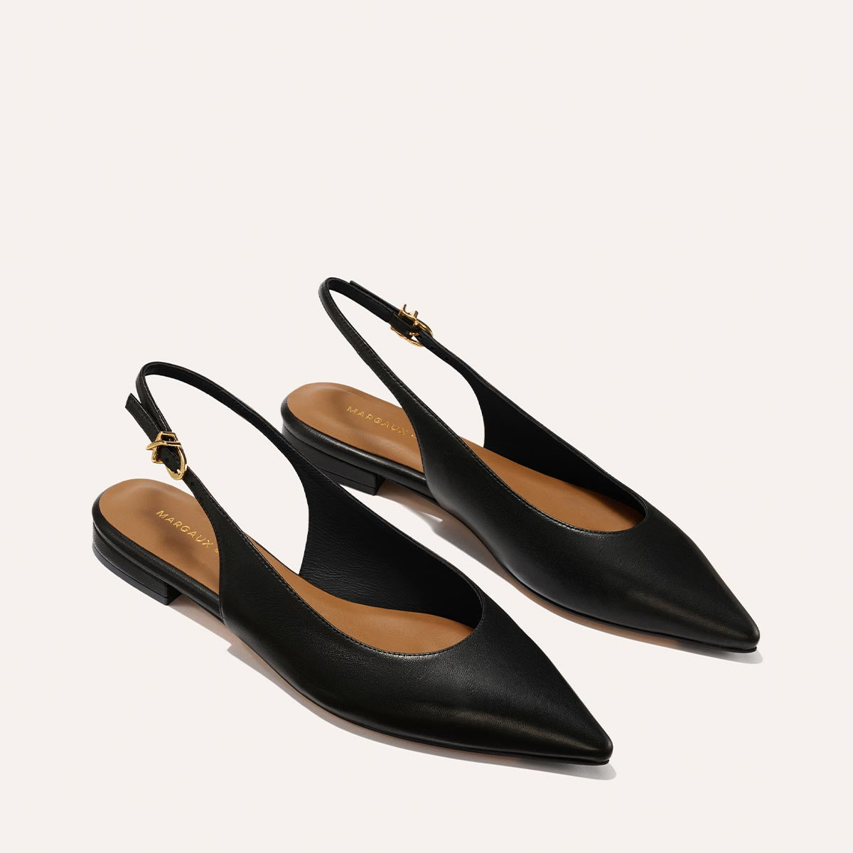 The Elise - Black Nappa flats by margaux-development feature a black pointed-toe slingback design, low heels, brown insoles, and adjustable ankle straps, shown against a light background.
