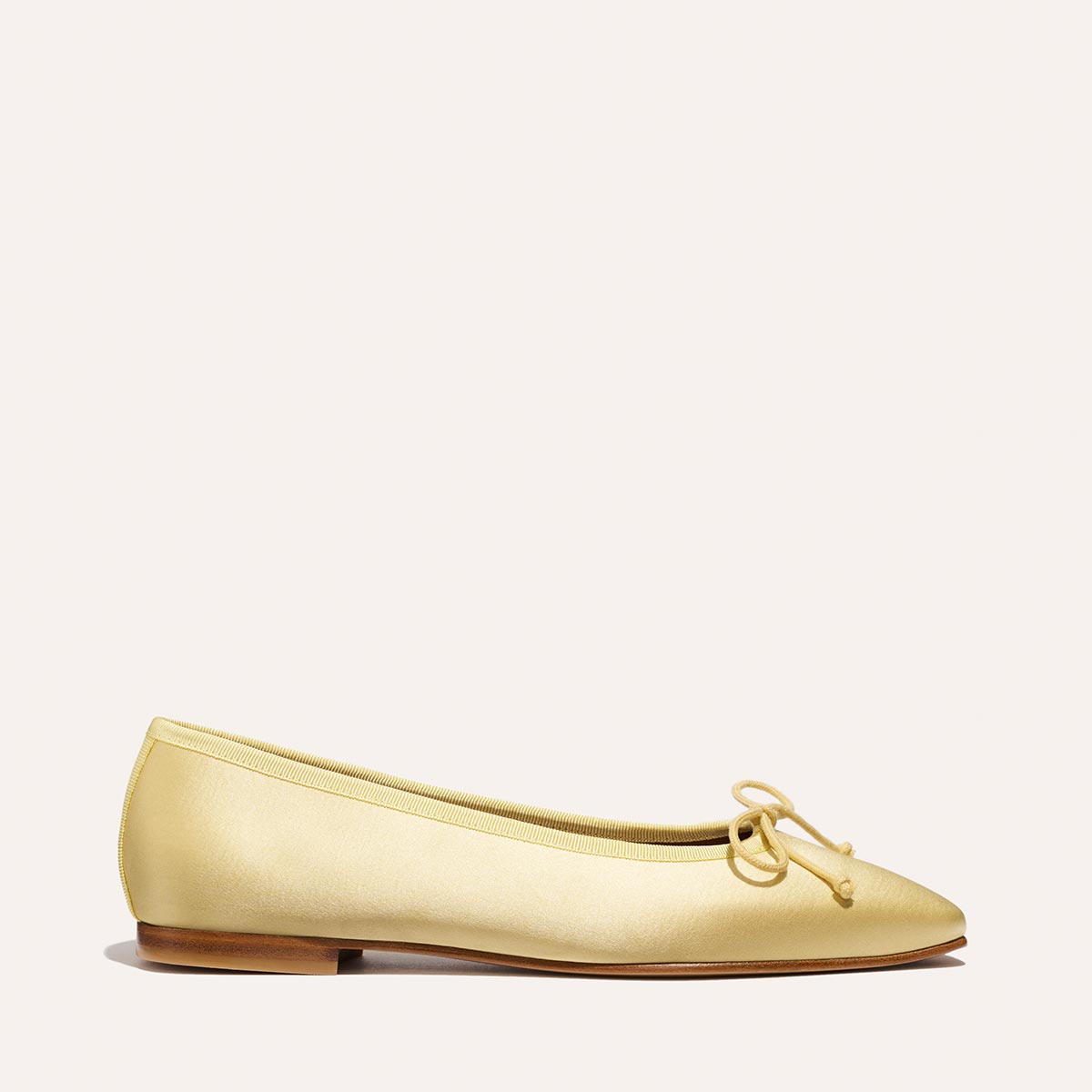 The Fonteyn - Butter Satin by Margaux is a comfort-first ballet flat in light yellow, featuring a small bow on the rounded toe, low wooden heel, and smooth matte finish. Displayed on a plain, light background.