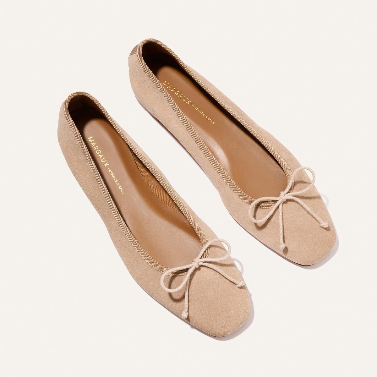 The Fonteyn - Cameo Suede by Margaux: beige suede ballet flats with square toes and decorative bows, shown on a white background.