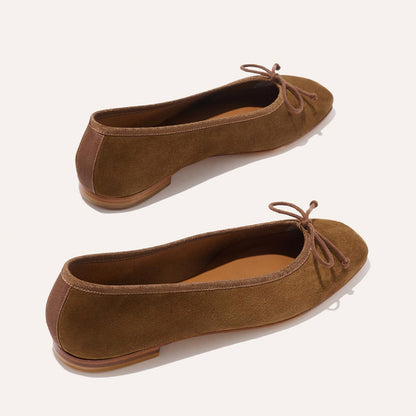 Margaux’s The Fonteyn - Cedar Suede ballet flats feature handcrafted brown suede, delicate front bows, brown soles, and gently rounded toes, elegantly displayed on a light background.