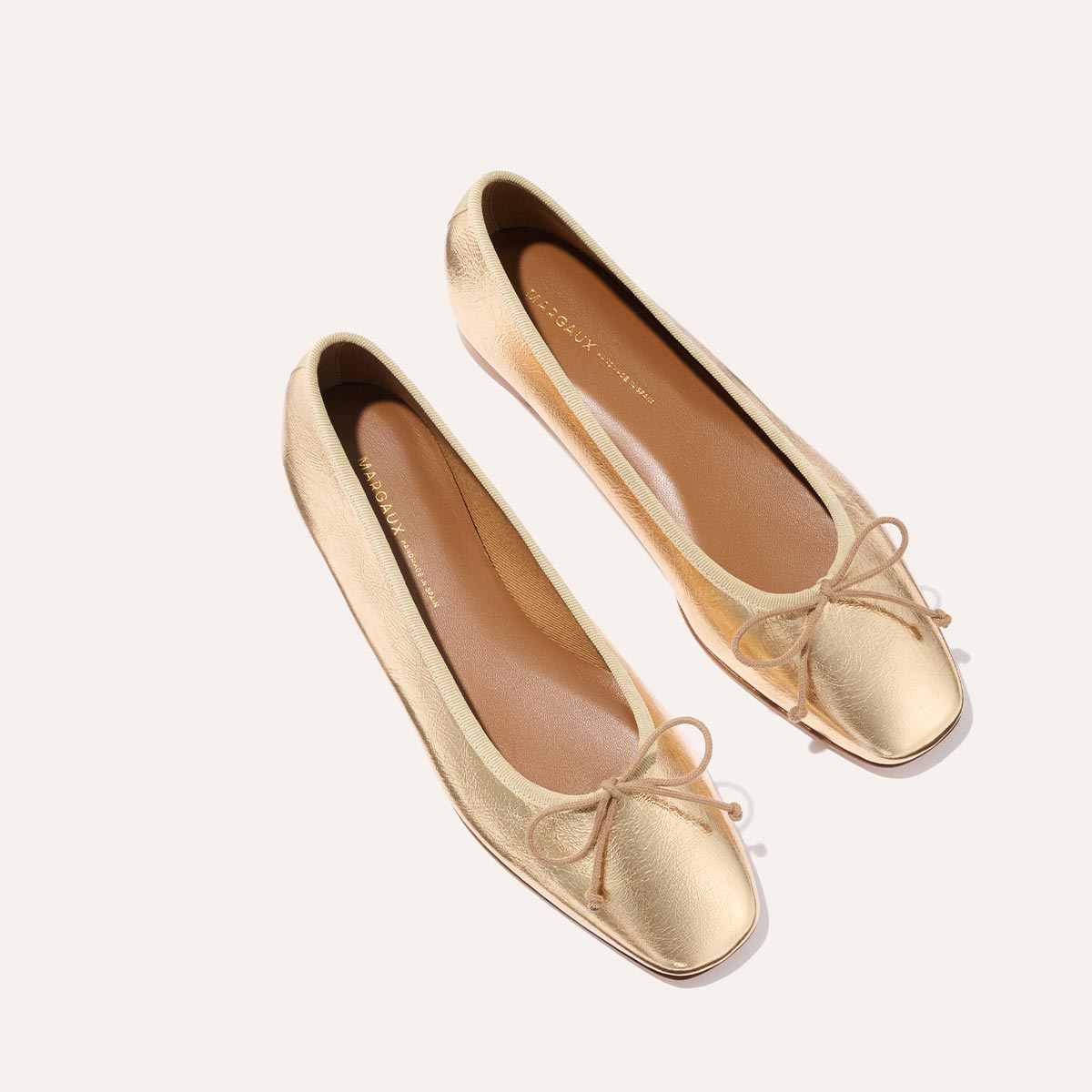 The Fonteyn - Gold Crinkle Nappa ballet flats by Margaux feature square toes and small front bows, displayed on a light background.