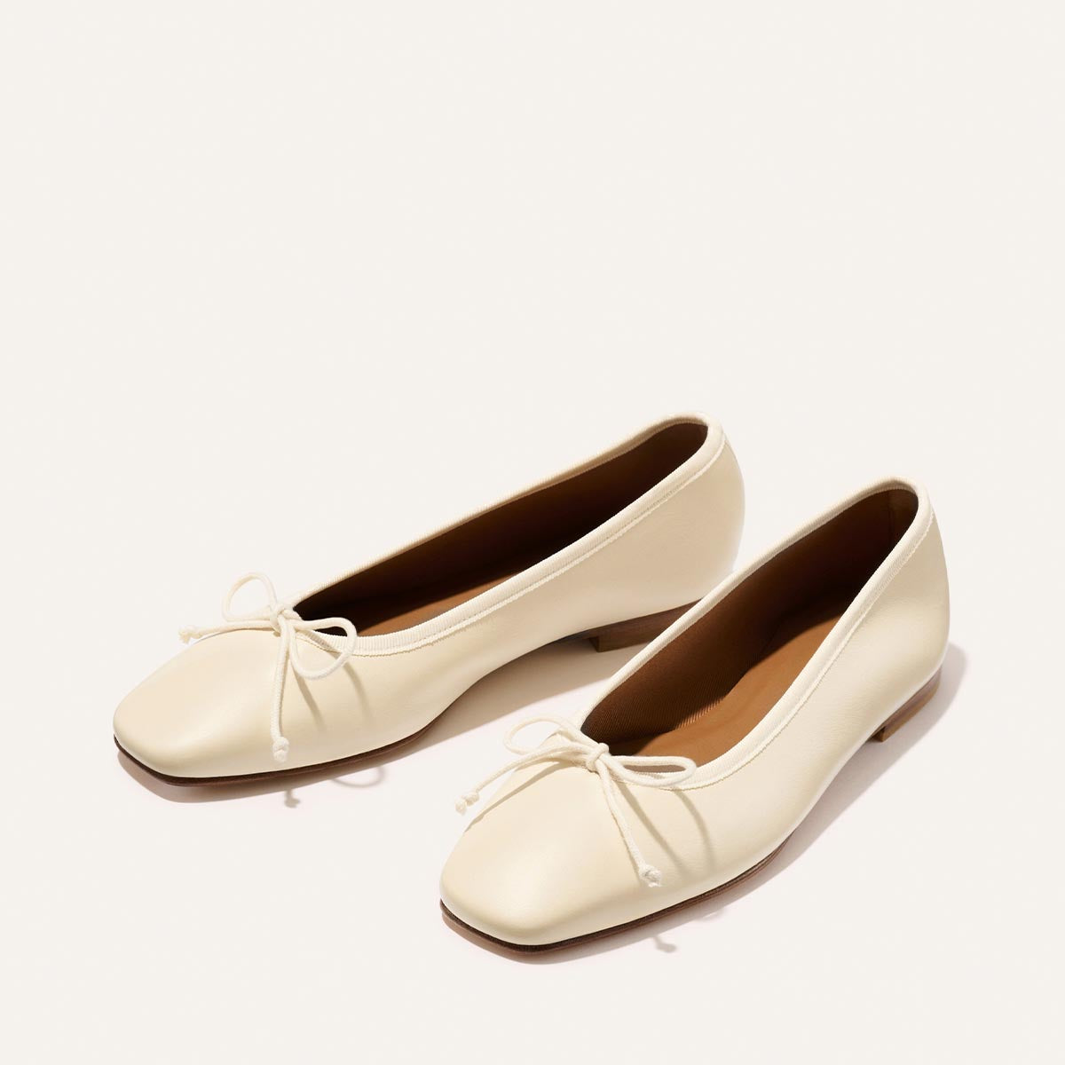Pair of cream-colored flat shoes with a bow on a light background