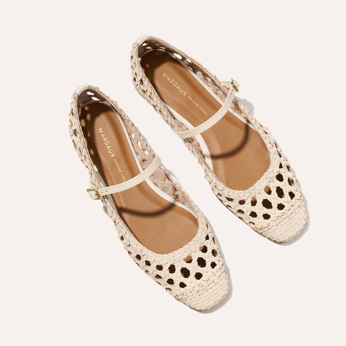 The Fonteyn Jane - Ecru Woven Leather by Margaux features cream-colored handwoven Mary Jane flats with closed toes, adjustable straps, and tan insoles. Displayed on a plain, light background.