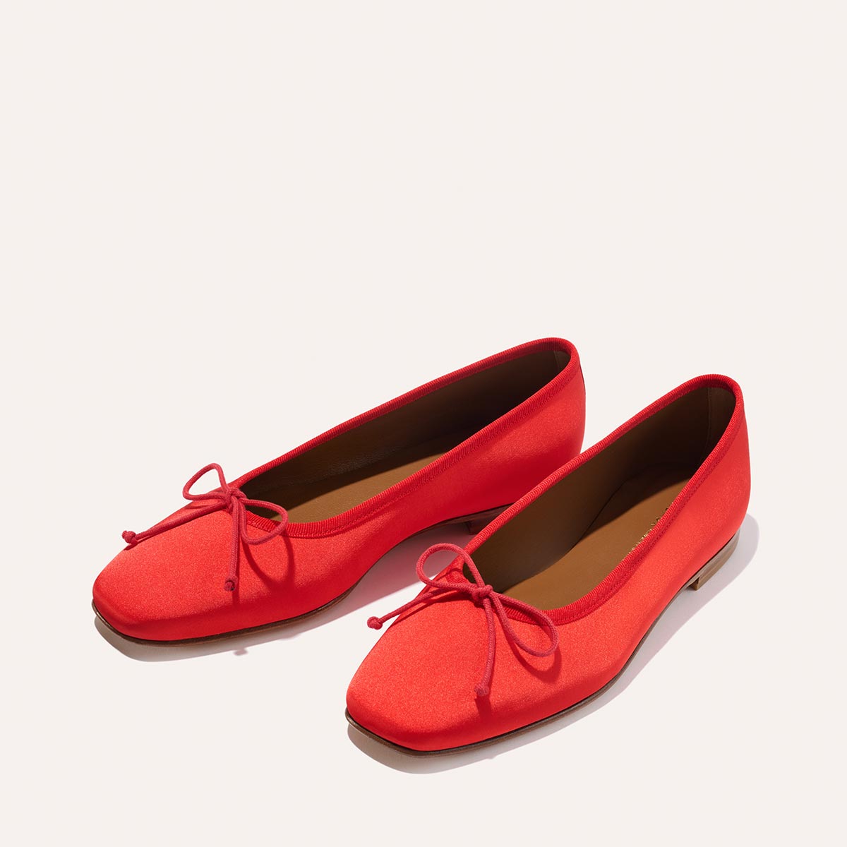 The Fonteyn - Poppy Satin by Margaux are bright red ballet flats with small toe bows, handcrafted for comfort with a classic, simple design and flat soles, displayed on a light background.