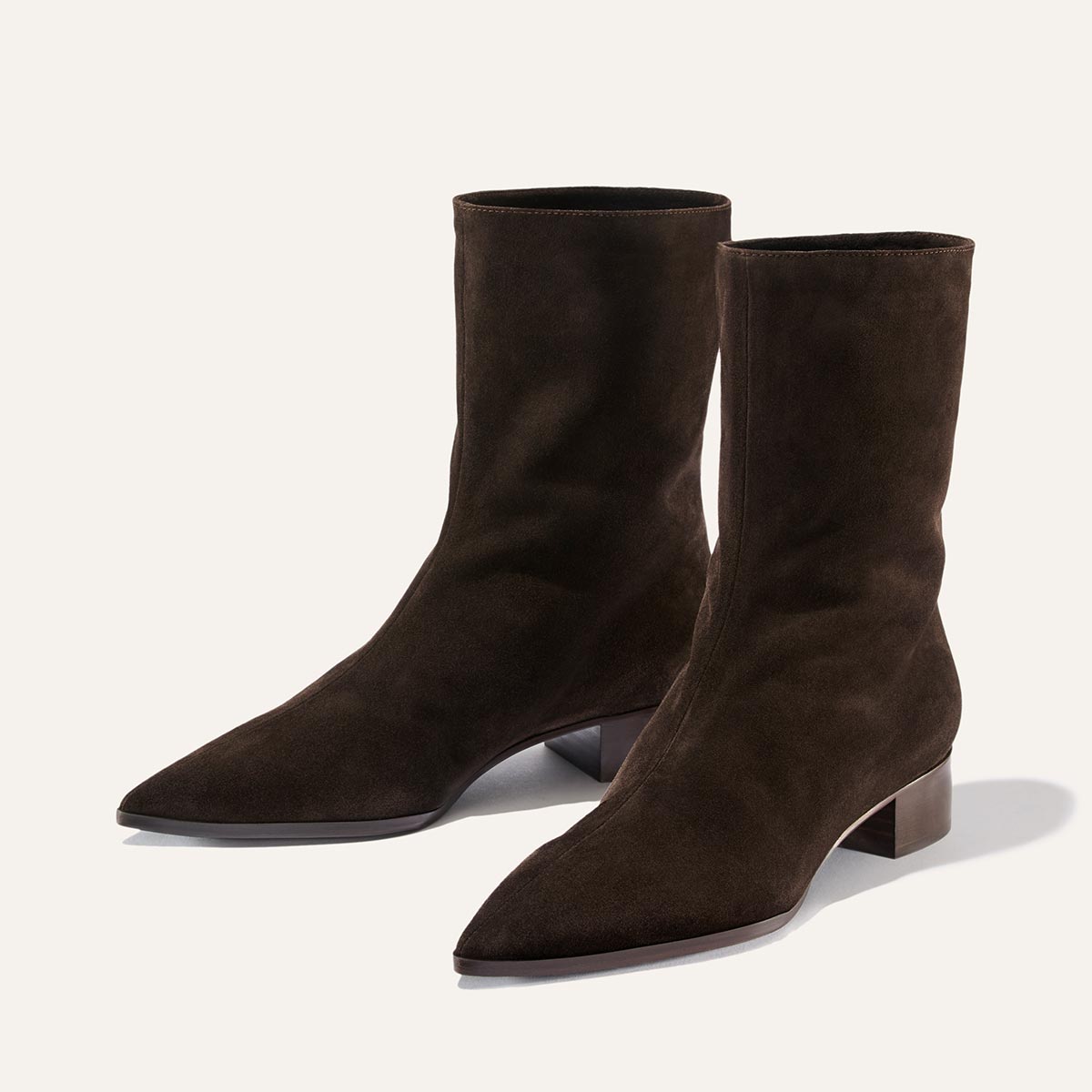 A pair of The Hayes Boot in Dark Chocolate Suede by Margaux, featuring pointed toes and low block heels, brings subtle bohemian flair, displayed on a plain light background.