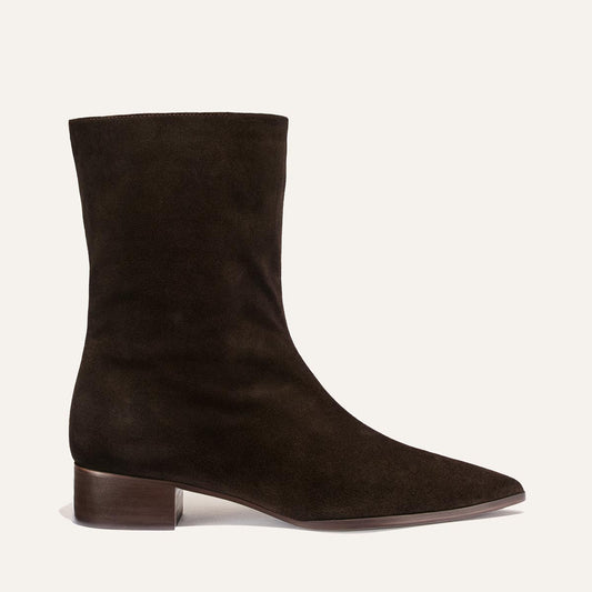 The Hayes Boot by Margaux in Dark Chocolate Suede features a low block heel and pointed toe, shown in side profile against a plain off-white background—an effortlessly versatile design that infuses subtle bohemian flair into every step.