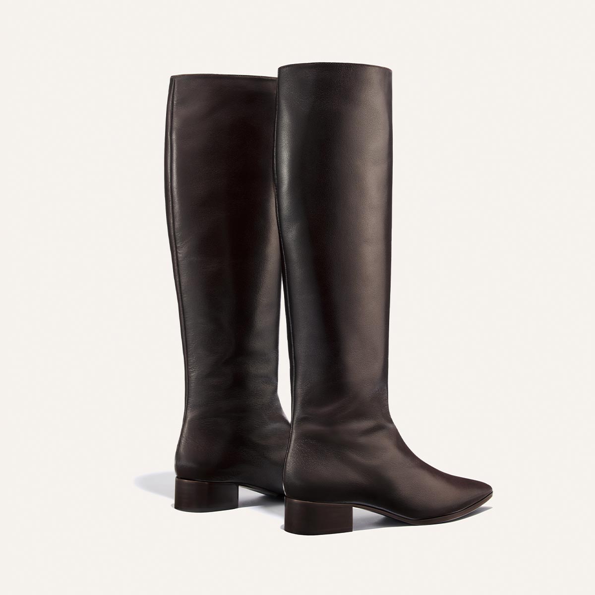 A pair of comfortable, handmade Margaux The Hayes Knee-High Boots in dark chocolate calf leather, featuring a low block heel, is positioned upright on a light background.