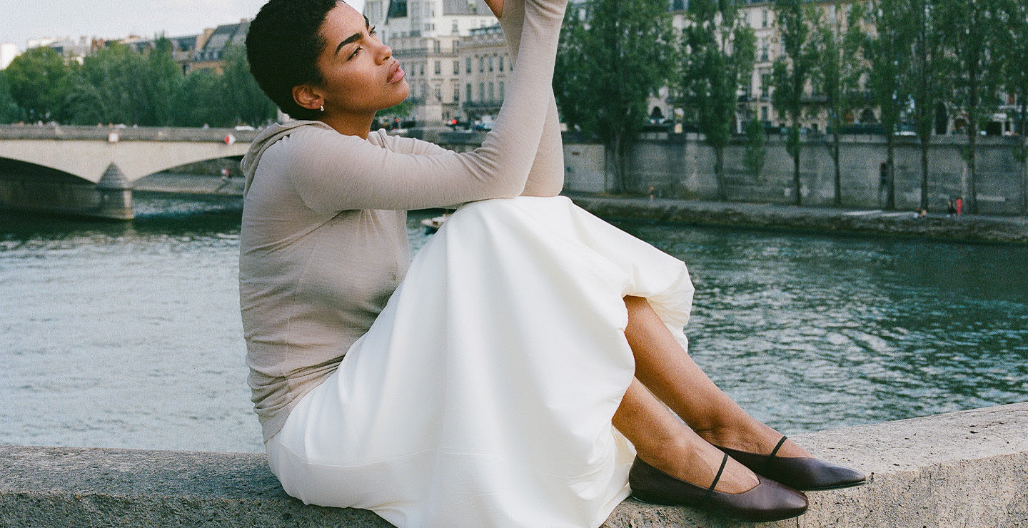 Woman in a white dress sitting by a river with a cityscape in the background