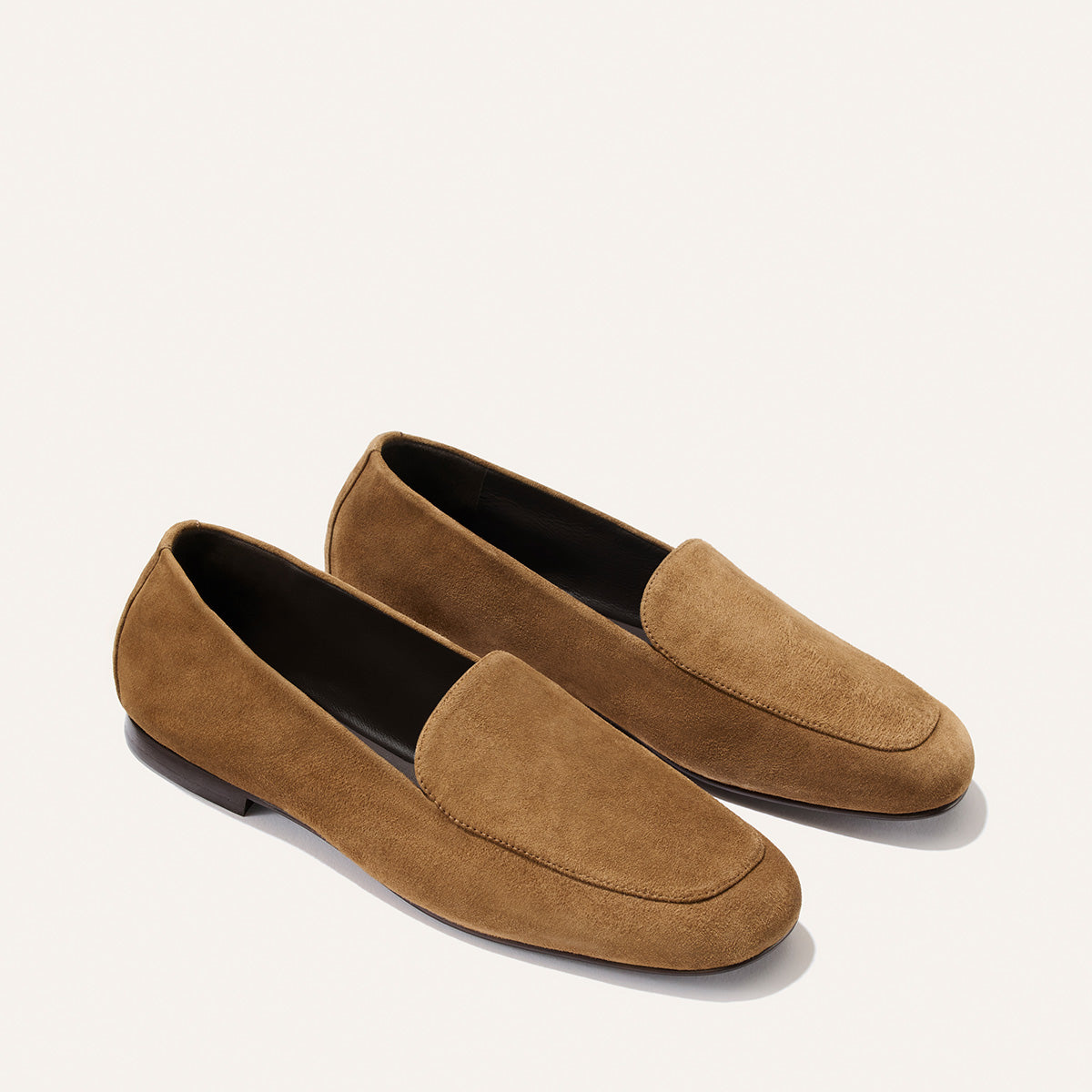 The James Loafer - Cedar Suede by Margaux, featuring brown suede with rounded toes and low black heels, crafted using sacchetto construction for a tailored fit, is displayed on a light background.