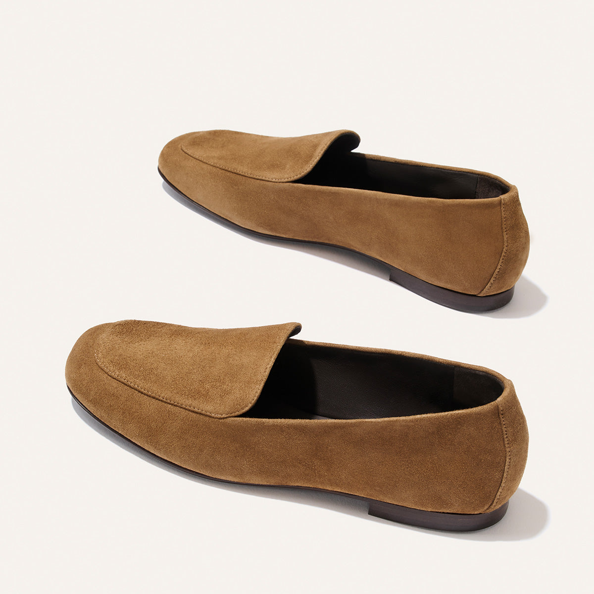 The James Loafer - Cedar Suede by Margaux is a pair of brown suede loafers featuring a minimalist design and flat dark soles, expertly crafted using sacchetto construction for a tailored fit and displayed on a light background.