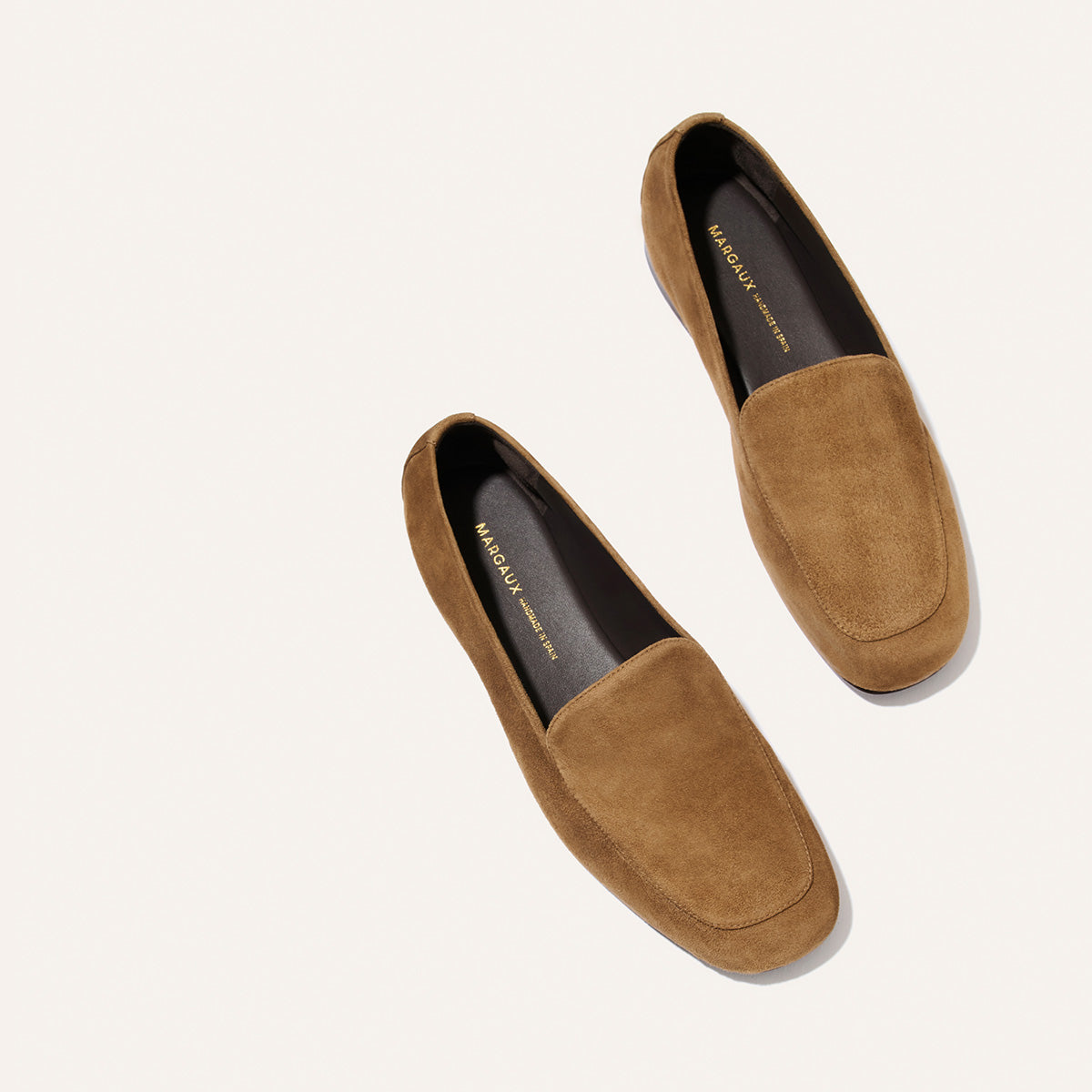 A pair of Margaux’s The James Loafer in Cedar Suede—brown suede loafers with dark insoles, handmade using sacchetto construction for a tailored fit—displayed slightly apart on a light beige background.