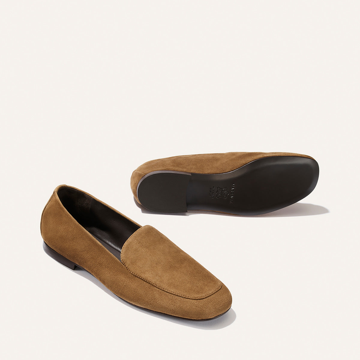 The James Loafer - Cedar Suede from Margaux is showcased, with one shoe standing upright and the other lying on its side to reveal the black sole. These handmade loafers offer a tailored fit, combining elegance and comfort in every step.