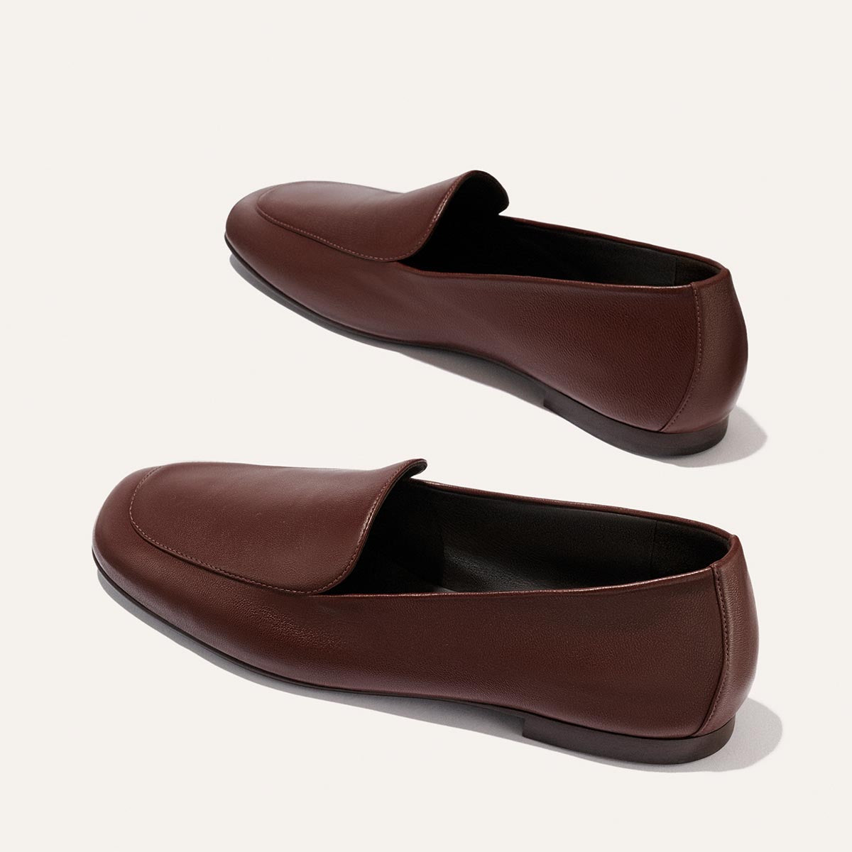 The James Loafer by Margaux in Mahogany Nappa is a pair of brown leather slip-on shoes with low heels, offering slippers-level comfort, displayed against a plain white background.