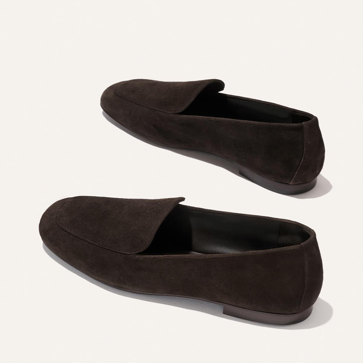 A pair of Margaux’s The James Loafer in Molasses Suede, featuring rounded toes and low heels, displayed on a light background and offering exceptional slipper-like comfort.
