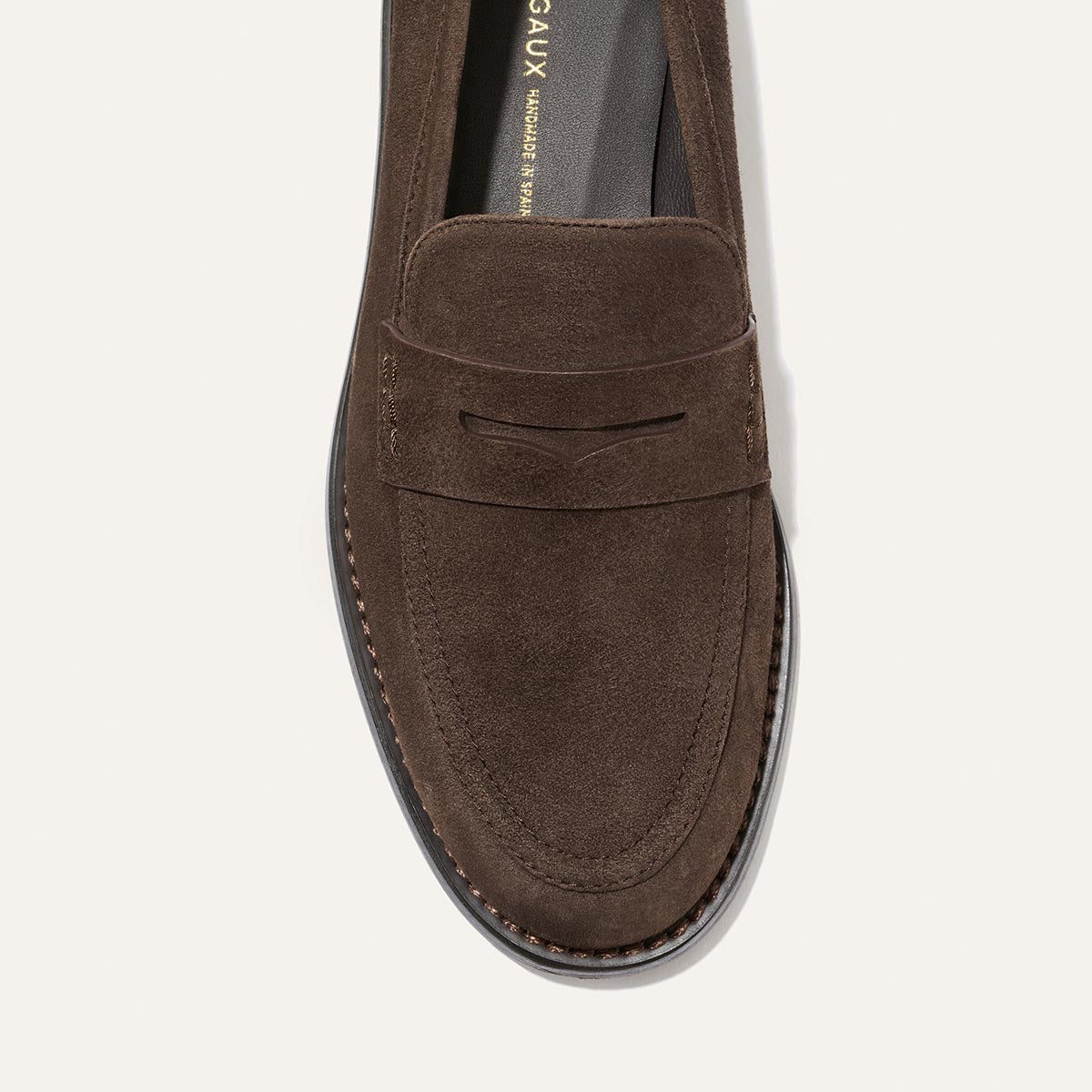 A top view of The Marlowe Loafer in Umber Suede by Margaux, a modern brown suede penny loafer featuring visible stitching and a black sole, set against a plain light background.