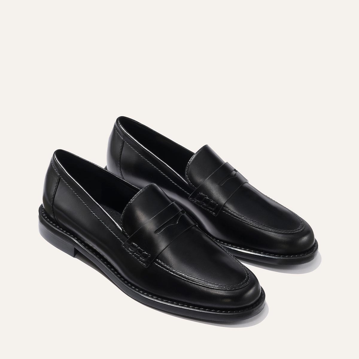 The Marlowe Loafer - Black Calf by margaux-development features classic black leather, rounded toes, low heels, a stitched seam around the upper, and a sleek polished finish. Both shoes are angled outward on a plain light background.