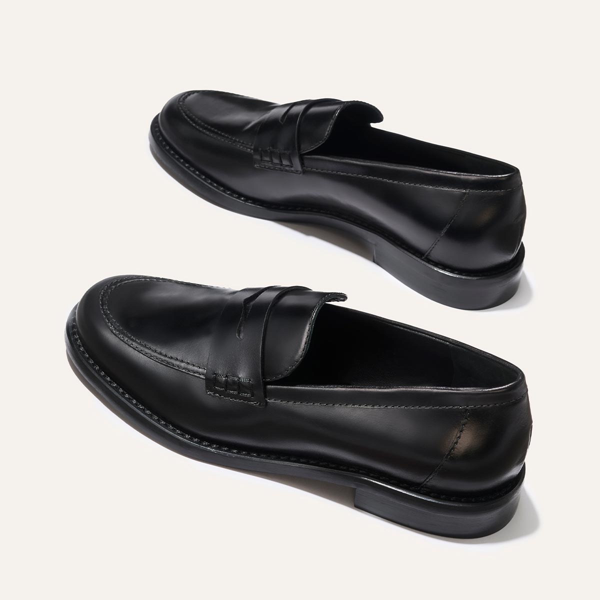 The Marlowe Loafer - Black Calf by margaux-development: black leather loafers with stitching details and low heels displayed on a light background, one upright and the other angled to show the side and sole.