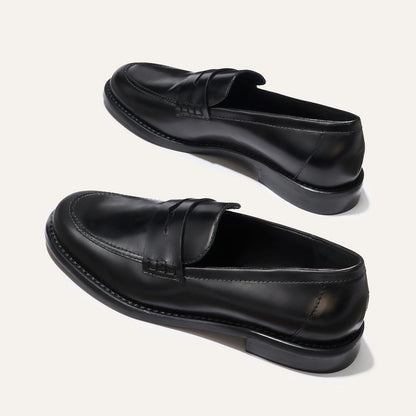 The Marlowe Loafer - Black Calf by margaux-development: black leather loafers with stitching details and low heels displayed on a light background, one upright and the other angled to show the side and sole.