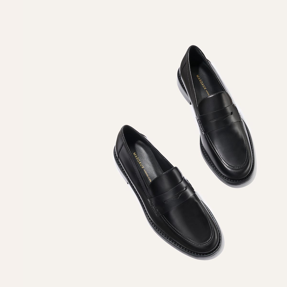 The Marlowe Loafer - Black Calf by margaux-development, featuring black leather with stitching detail and a low heel, is shown positioned diagonally on a plain light background.