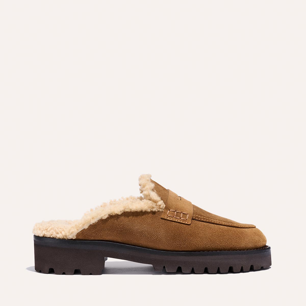 The Marlowe Mule by Margaux features walnut suede, cream shearling lining, and a chunky black sole, shown in profile against a plain light background.