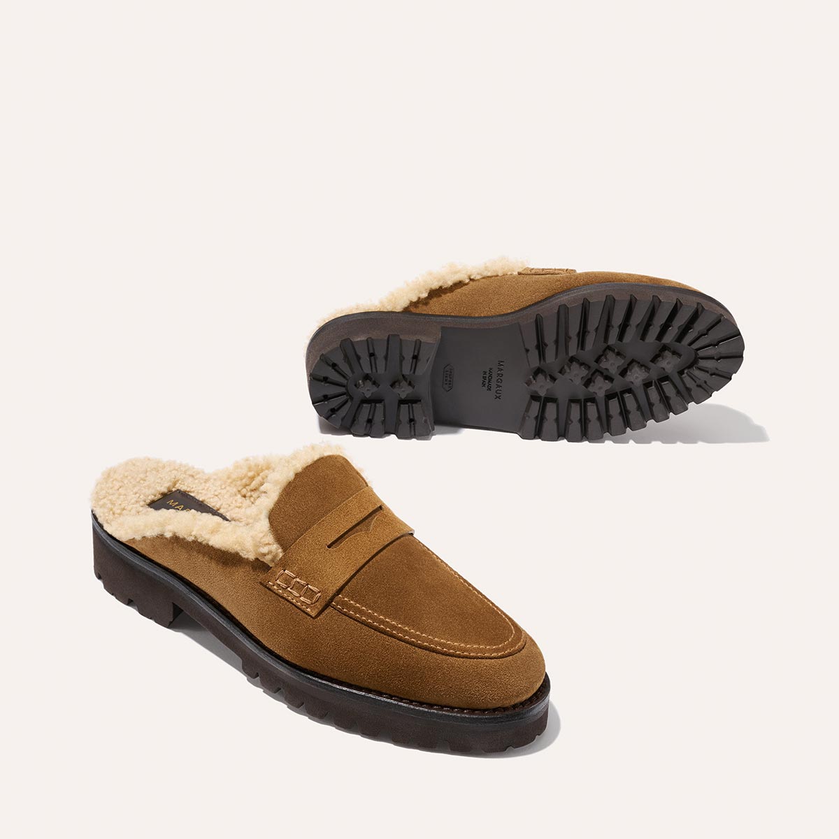 The Marlowe Mule by Margaux in walnut suede features a fluffy cream shearling lining and rugged black treaded soles, shown against a light background.