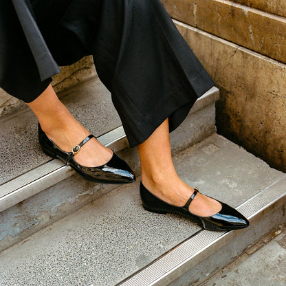 The Mary Jane in Black Patent, a ballet flat with a pointed toe and an adjustable strap for a secure fit.