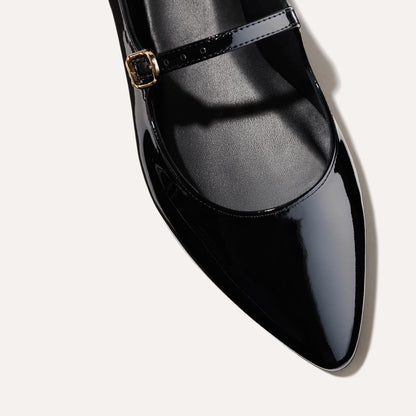 The Mary Jane in Black Patent, a ballet flat with a pointed toe and an adjustable strap for a secure fit.