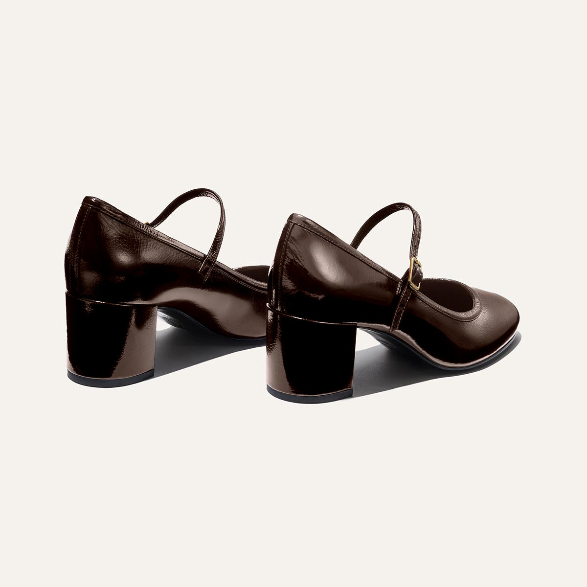 The Mira Jane - Cocoa Crinkle Patent by margaux-development: shiny dark brown patent Mary Jane shoes with low block heels and thin straps, displayed on an off-white background.