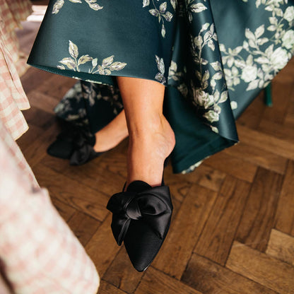 The Mule in Black Grosgrain, a slip-on silhouette featuring a pointed toe and oversized bow detail. 