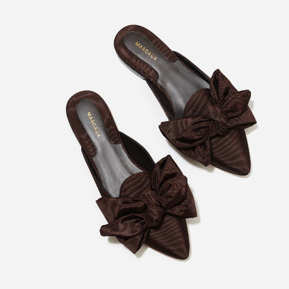 The Mule in Espresso Moire, a slip-on silhouette featuring a pointed toe and oversized bow detail. 