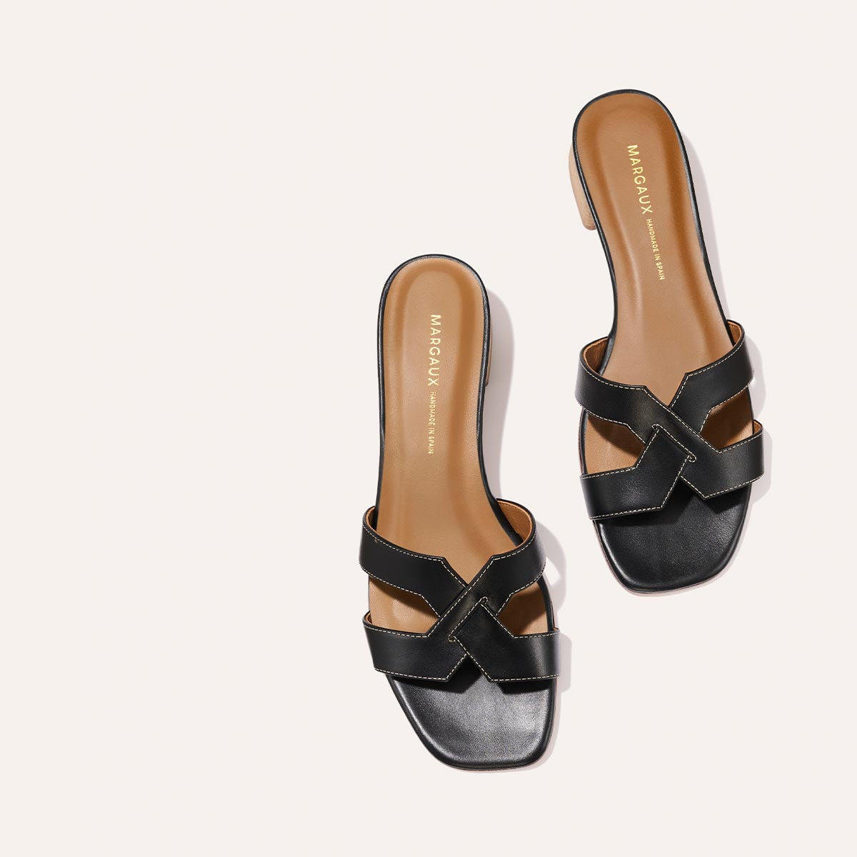 The MX 35 - Black Calf by Margaux-development: black leather slide sandals with crisscross straps, tan insoles, a square toe, visible edge stitching, and a comfortable block heel. Displayed on a light background.