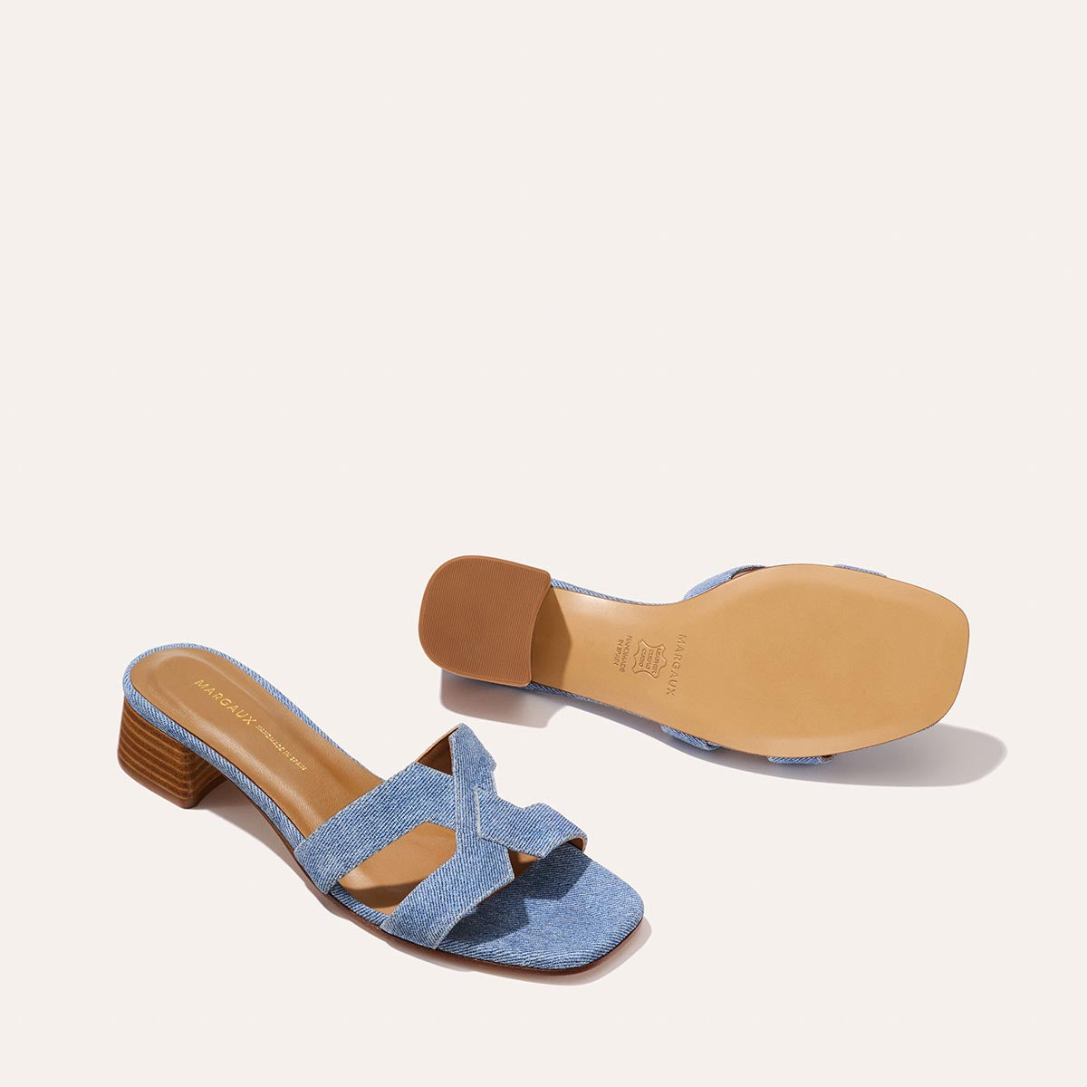 A pair of Margaux-development The MX 35 - Denim Suede women’s open-toe sandals featuring light blue crisscross straps, a walkable low brown block heel, and a tan sole. One sandal is upright; the other displays the bottom.