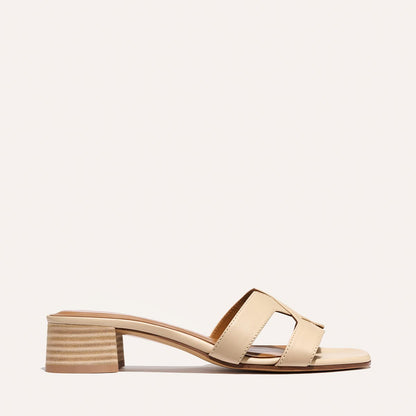The MX 35 - Latte Calf by Margaux is a beige open-toe sandal with two wide cutout straps and a low block heel. Its minimalist, modern style stands out against a simple, light backdrop.