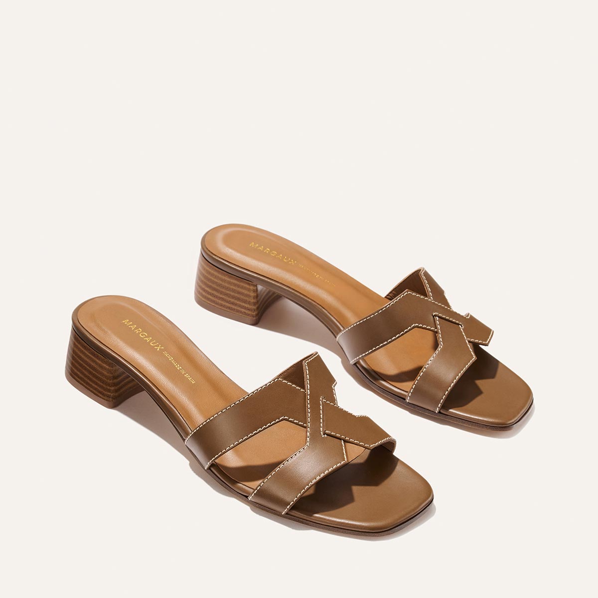 The MX 35 - Mocha Calf by Margaux: chic brown heeled sandals with crisscross leather straps, contrast stitching, a low block heel, and open toe design, shown on a light background.